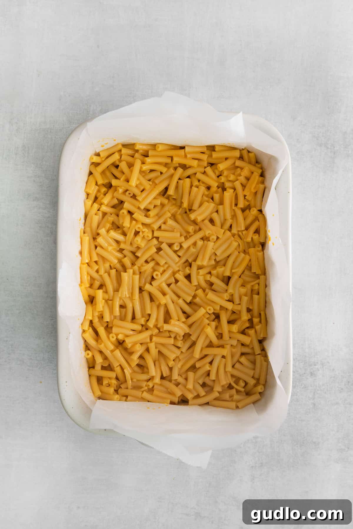 Creamy, golden macaroni and cheese expertly spread into a parchment-lined casserole dish, ready for chilling.