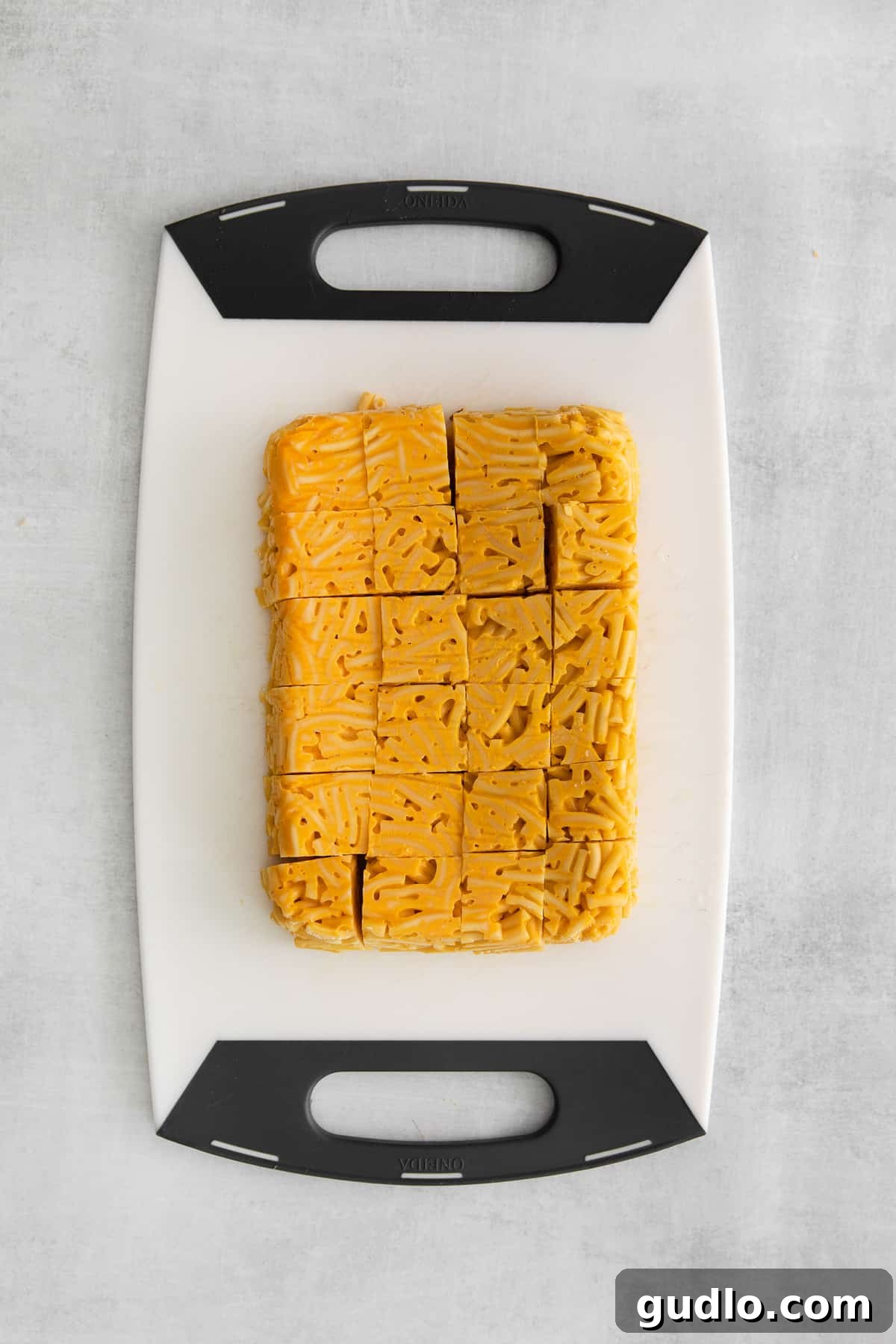Precisely cut 1x1-inch cubes of chilled mac and cheese neatly arranged on a wooden cutting board, ready for the next step in the recipe.