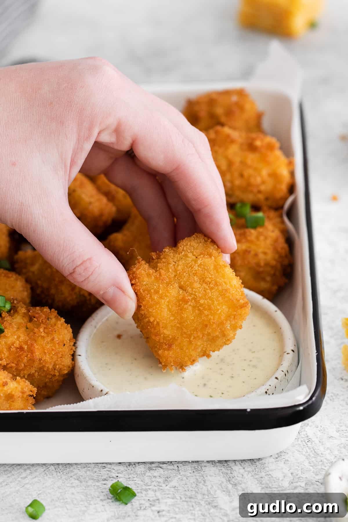 A hand gently dipping a golden-fried mac and cheese bite into a small bowl of creamy ranch dressing, emphasizing the delicious pairing.