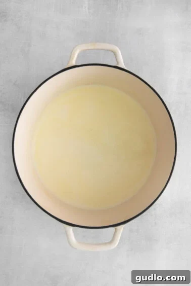 Velvety Cheddar Delight 5 Creamy liquid base of the soup being whisked in a white pot, lump-free and smooth.