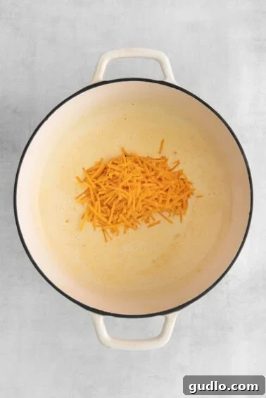Velvety Cheddar Delight 6 Melted cheddar cheese being stirred into the creamy soup base in a pan.