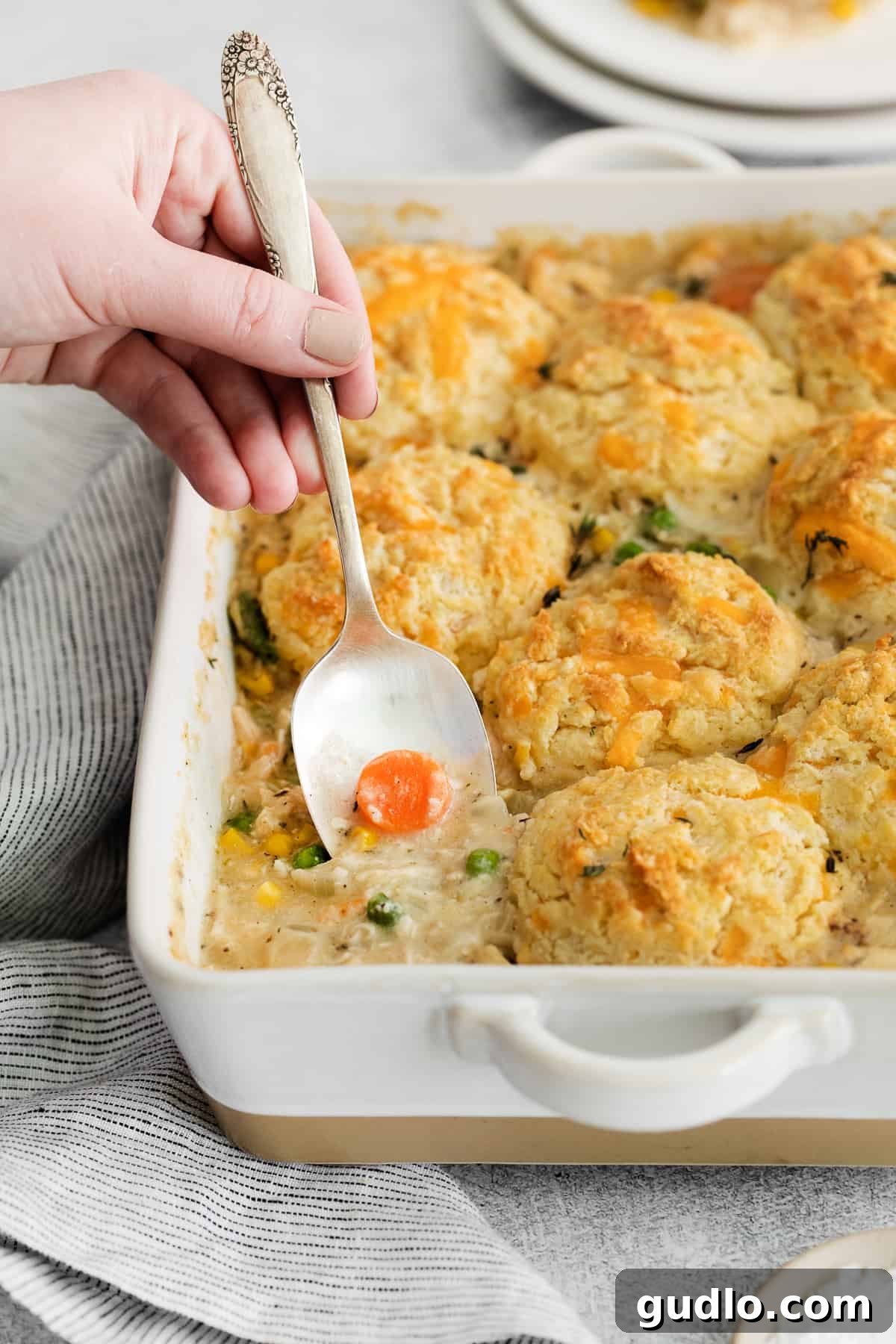 Scooping out a generous portion of creamy chicken pot pie casserole topped with golden brown cheddar biscuits.