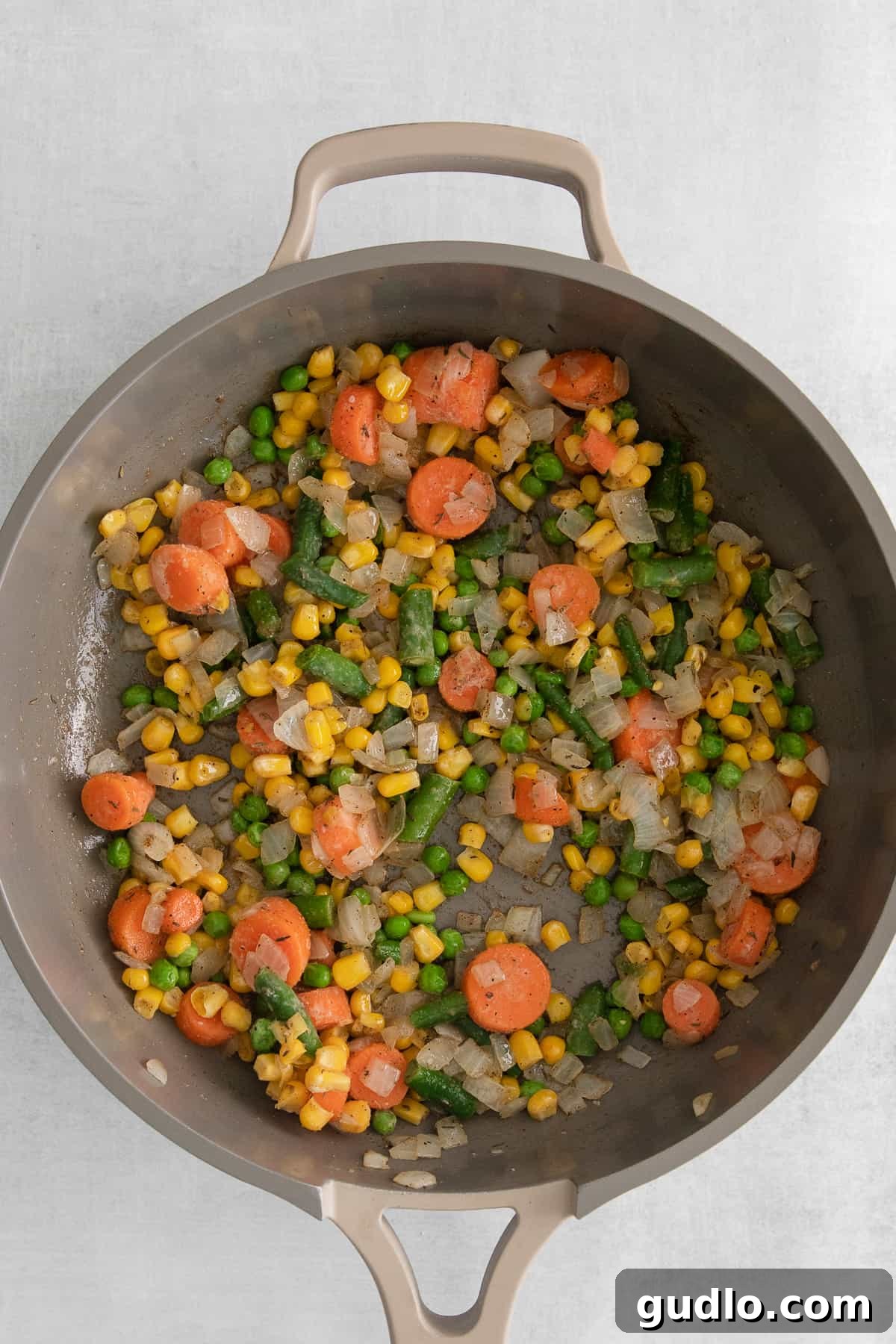 Close-up shot of colorful mixed vegetables, including carrots, peas, and green beans, cooking in a pan.
