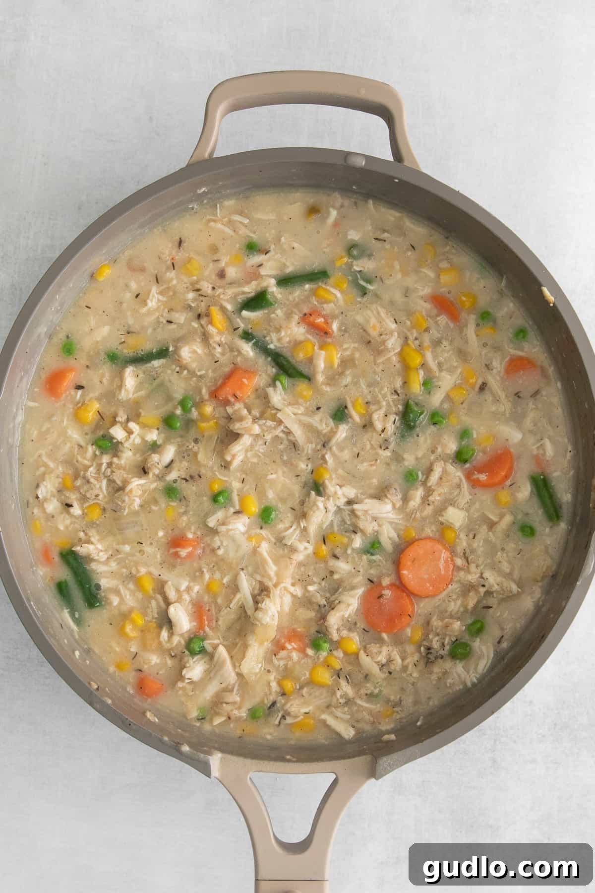 Rich and creamy chicken pot pie filling, generously packed with chicken and vegetables, simmering in a large skillet.