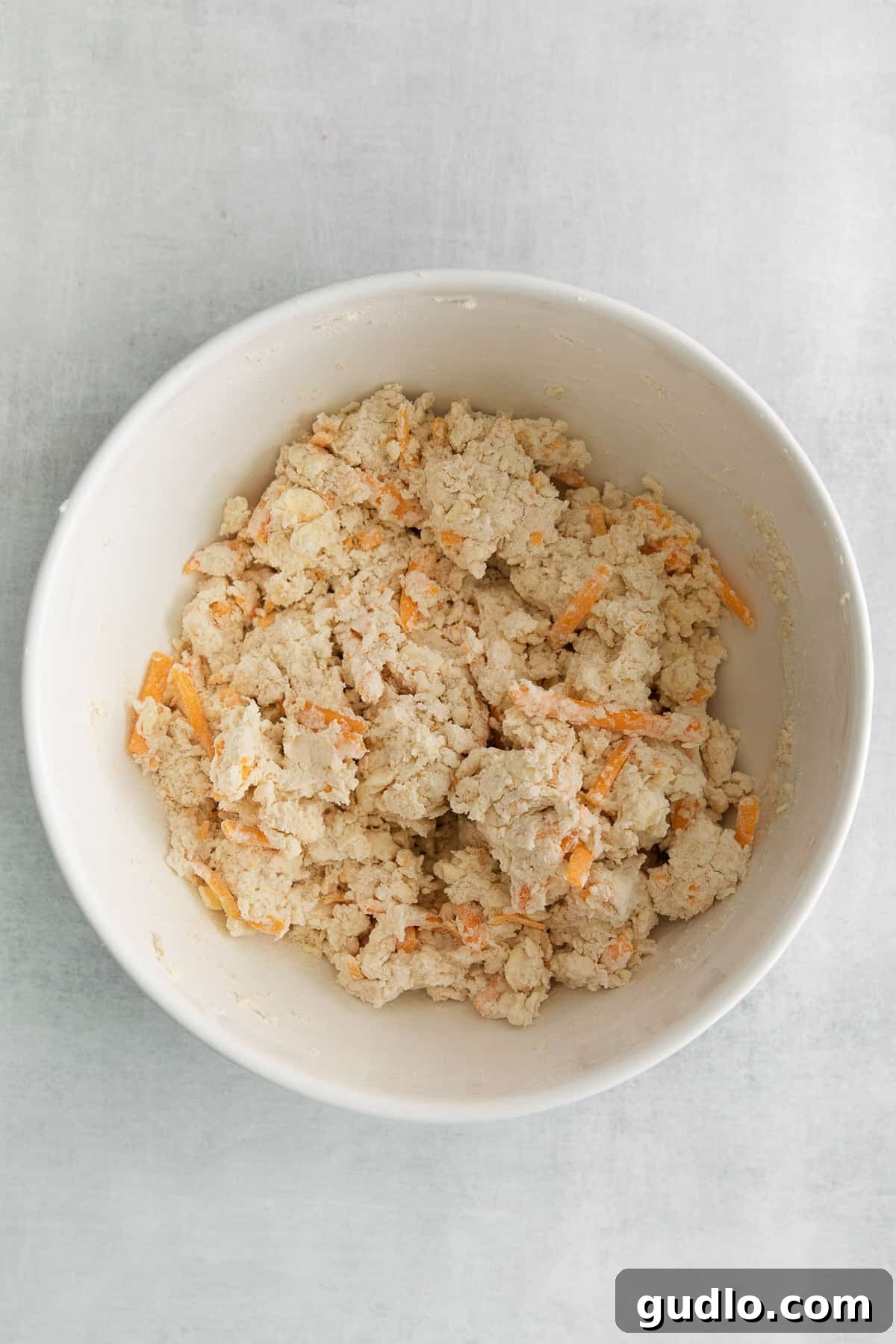 Bowl of freshly prepared cheddar biscuit dough, ready to be scooped and baked, showing the specks of cheddar cheese.