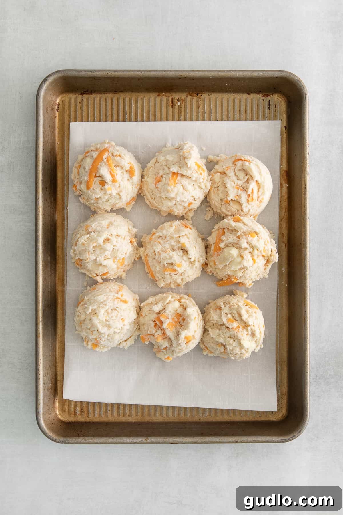 Uncooked cheddar biscuits, perfectly shaped and ready for the oven, laid out on a baking sheet lined with parchment paper.