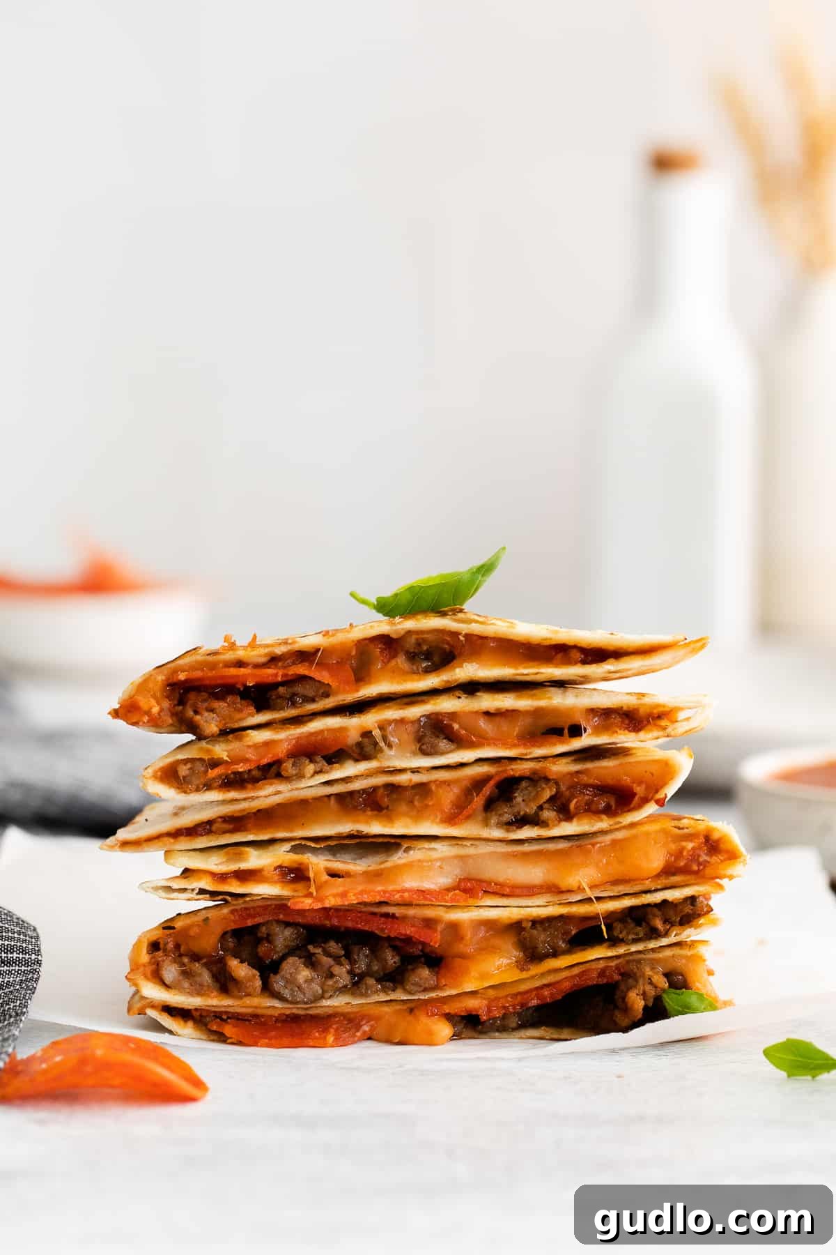 Pizza-Dilla Delight 2 Pizza quesadilla stacked on a plate, garnished with fresh basil.