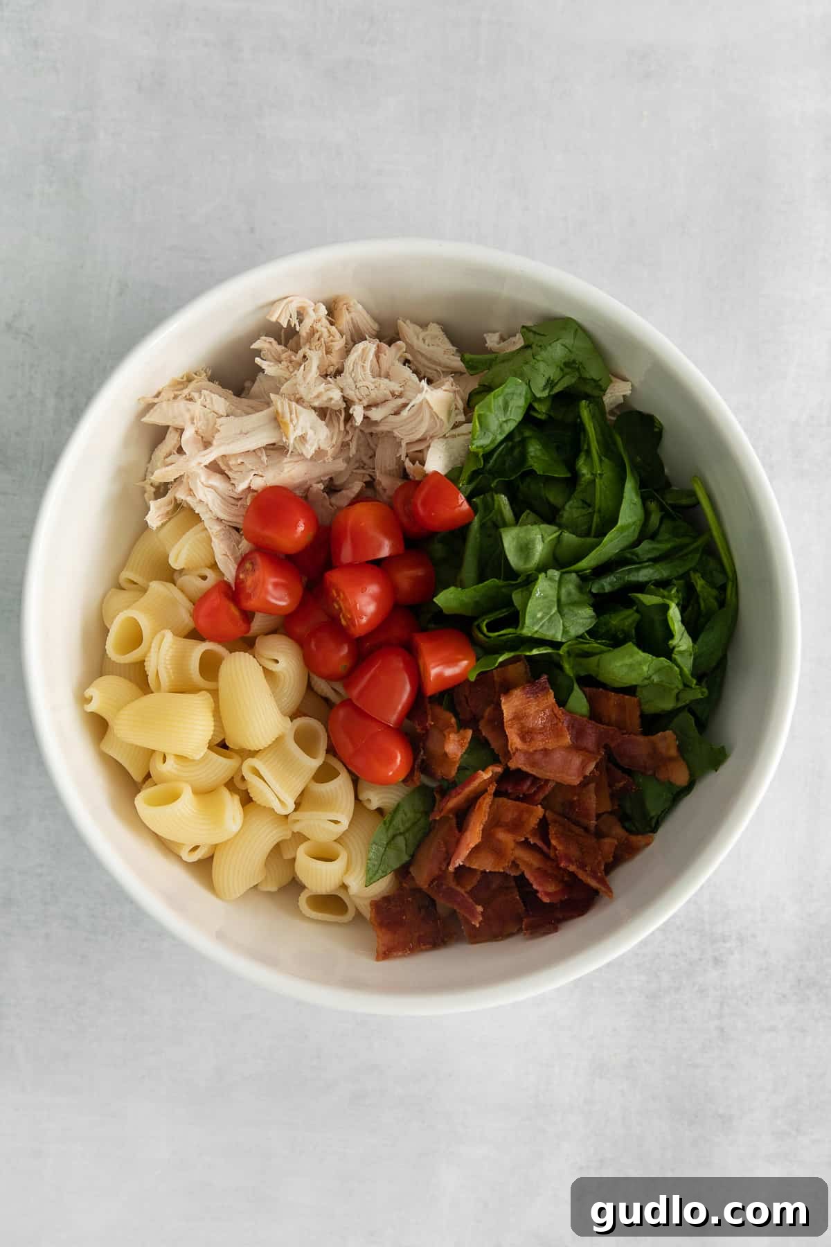 Creamy Gorgonzola Chicken Pasta Salad 4 A large mixing bowl containing a colorful assortment of pasta, shredded chicken, fresh spinach, crispy bacon, and halved cherry tomatoes, waiting for the dressing.