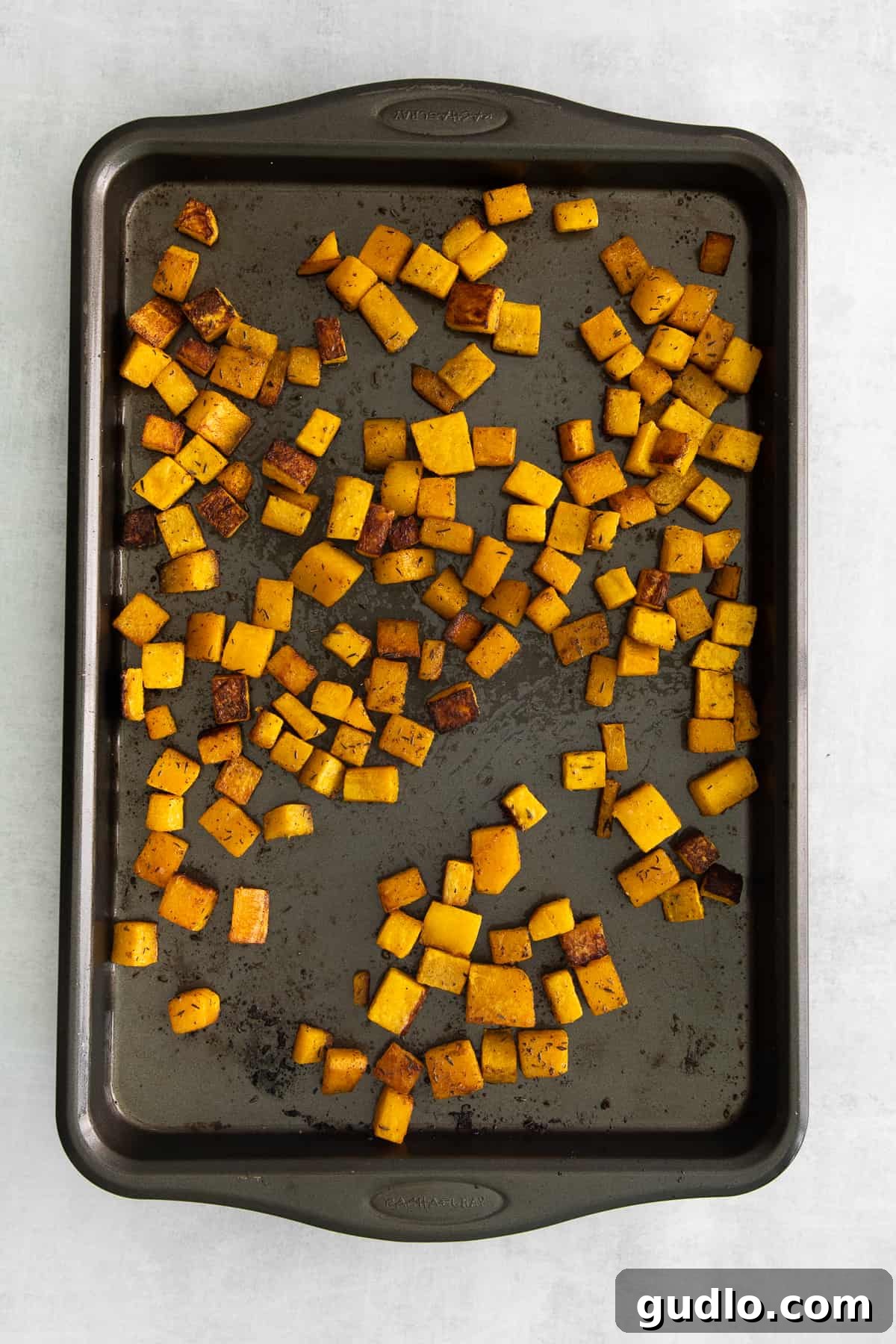 Freshly cubed pie pumpkin seasoned with spices on a baking sheet, ready for roasting.