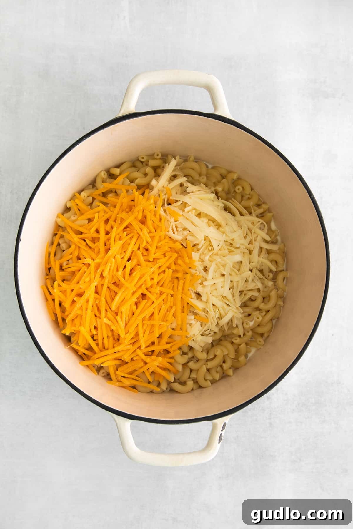 Uncooked elbow macaroni noodles topped with freshly shredded cheddar and Gruyere cheese in a large Dutch oven.