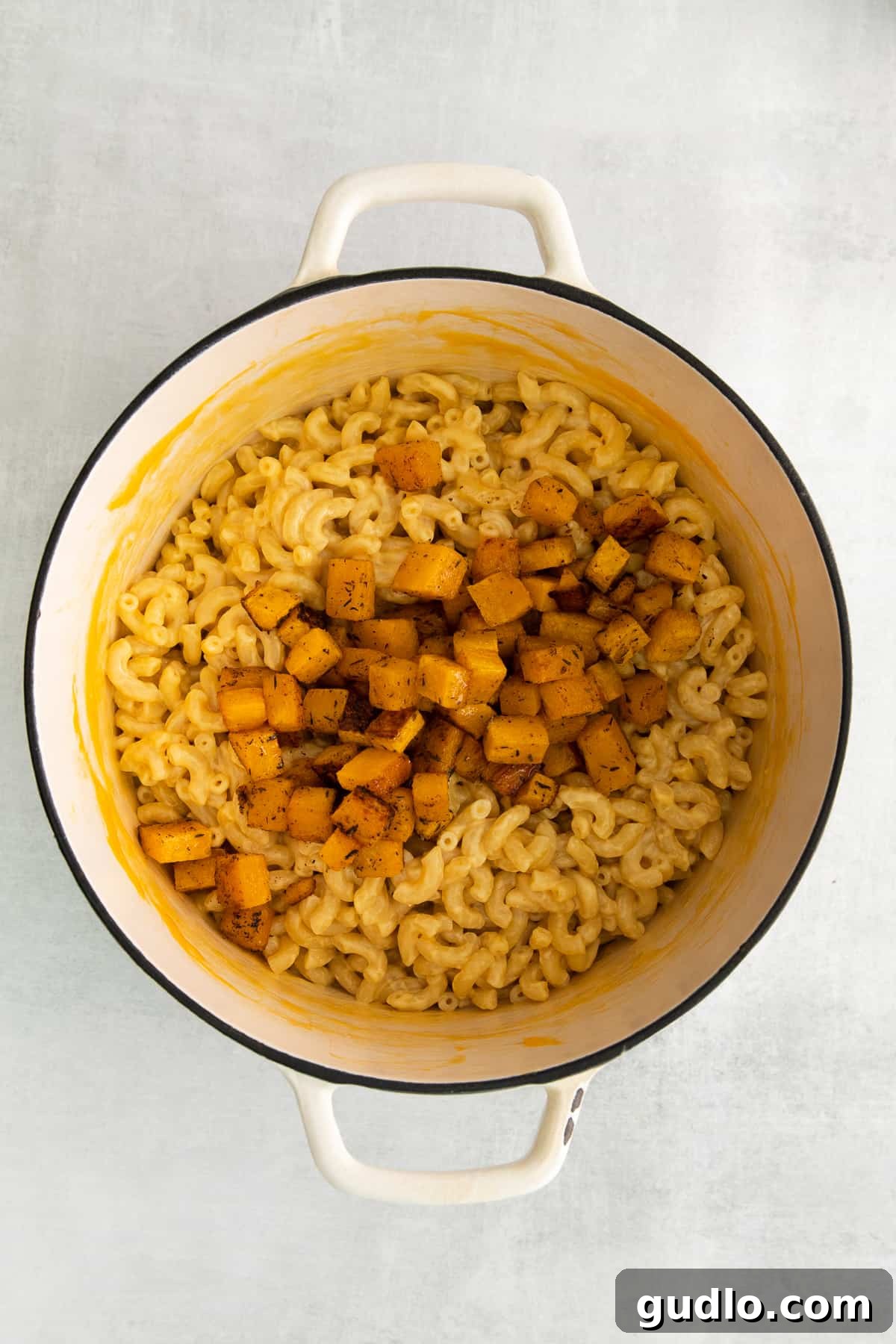 Rich pumpkin mac and cheese served in a cast iron pot, garnished with fresh herbs.