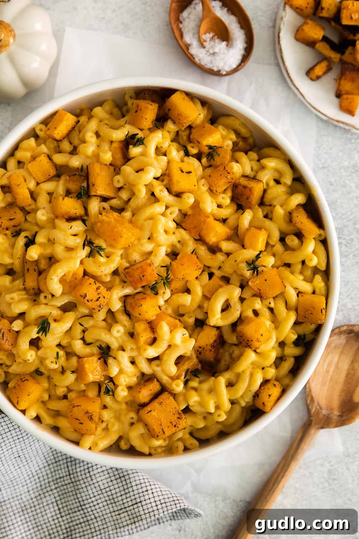 A generous serving of pumpkin mac and cheese in a white ceramic bowl, garnished with fresh thyme.