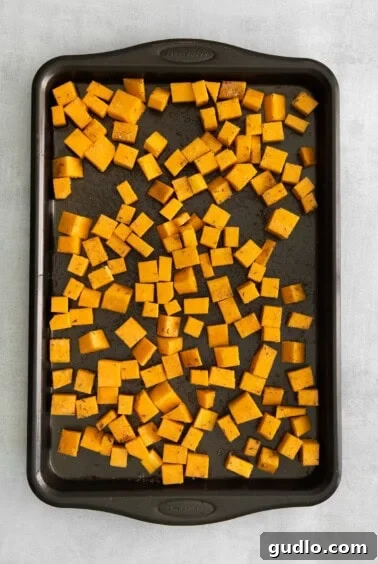 Seasoned pumpkin cubes on a baking sheet, ready for roasting.
