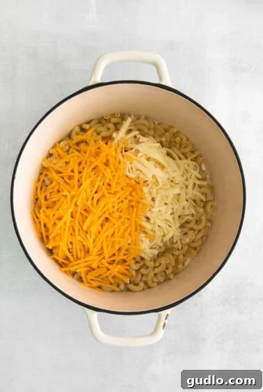 Shredded cheese melting into pasta and cream in a Dutch oven.