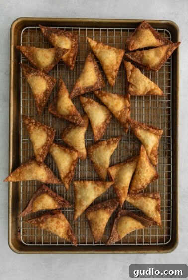 Crispy Creamy Crab Puffs 5 Freshly fried rangoons resting on a baking sheet lined with paper towels, draining excess oil and maintaining crispiness.