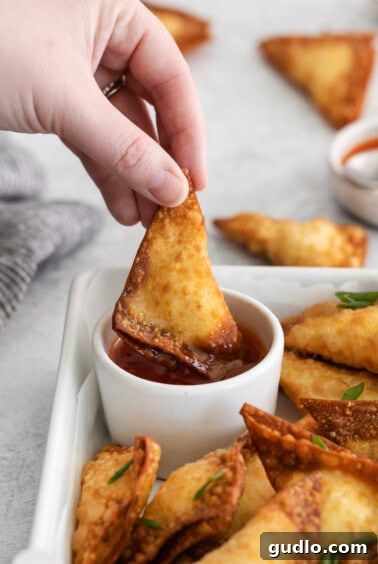 Crispy Creamy Crab Puffs 6 A delicious crab rangoon being dipped into a small bowl of savory sauce, ready to be enjoyed as a perfect appetizer.