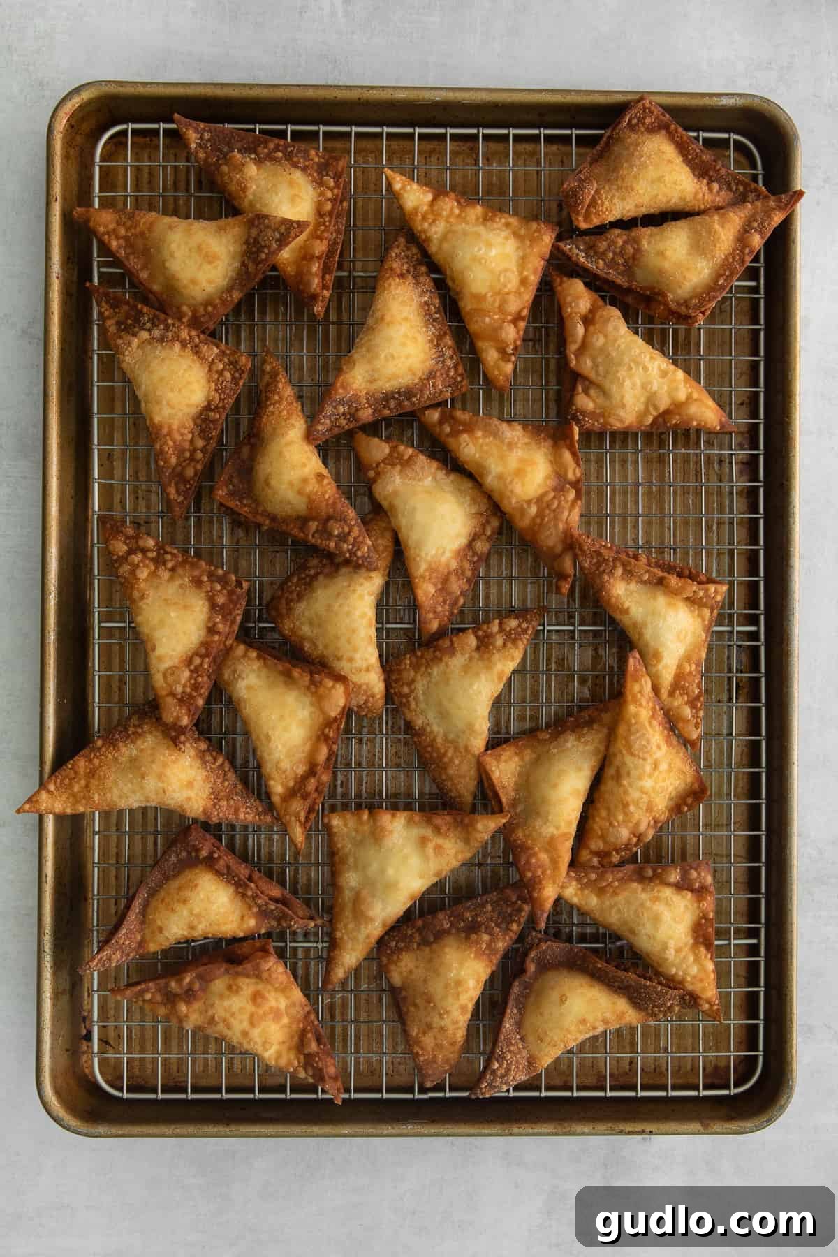 Freshly Fried Crab Rangoons Draining A batch of freshly fried crab rangoons draining on a wire rack lined with paper towels, showcasing their even golden crisp.