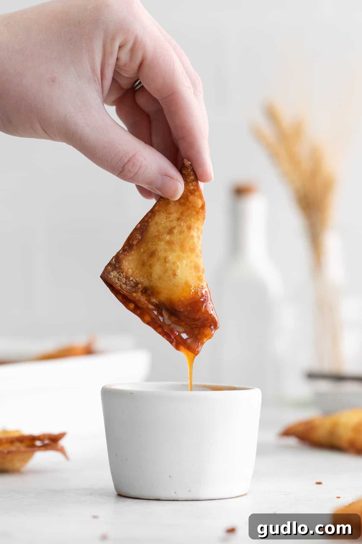 Dipping Crab Rangoon in Sauce A freshly fried crab rangoon being carefully dipped into a small bowl of vibrant sweet and sour sauce, emphasizing its crispy edges and perfect golden color.