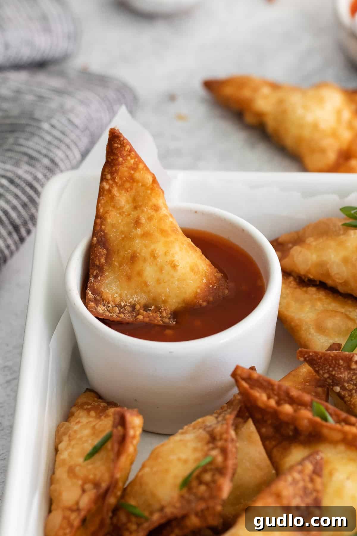 Crab Rangoon and Dipping Sauce Another alluring view of a crispy crab rangoon being dipped into a small bowl of vibrant sauce, perfectly highlighting its appetizing texture and golden hue.