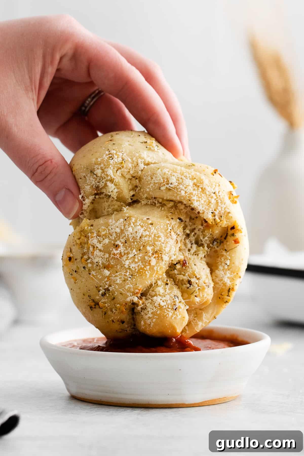 Dipping a freshly baked Parmesan garlic knot into a vibrant red marinara sauce, highlighting its soft texture and golden crust.