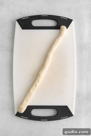 A hand shaping dough into a 10-inch rope, an essential step before tying the knots.