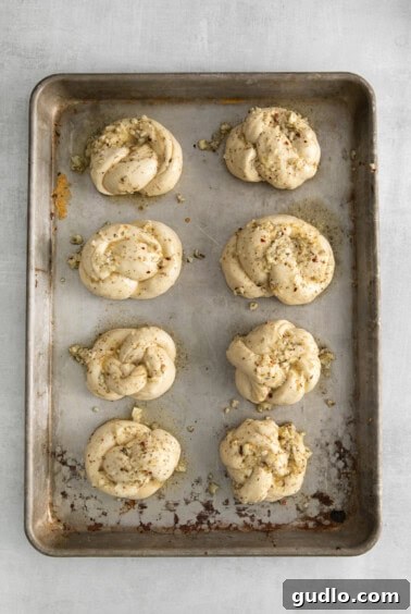 Garlic knots on a baking sheet, brushed generously with butter and spices, ready for the oven.