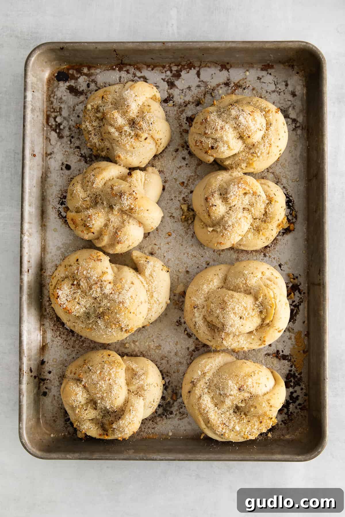 Freshly baked Parmesan garlic knots, perfectly golden-brown and glistening with melted butter, on a baking sheet.