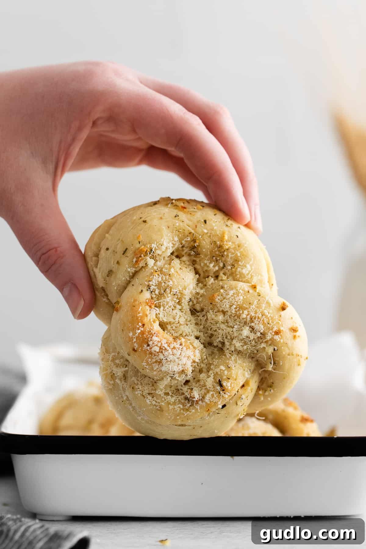 A hand holding a single, perfectly baked Parmesan garlic knot, showcasing its delicious appeal.
