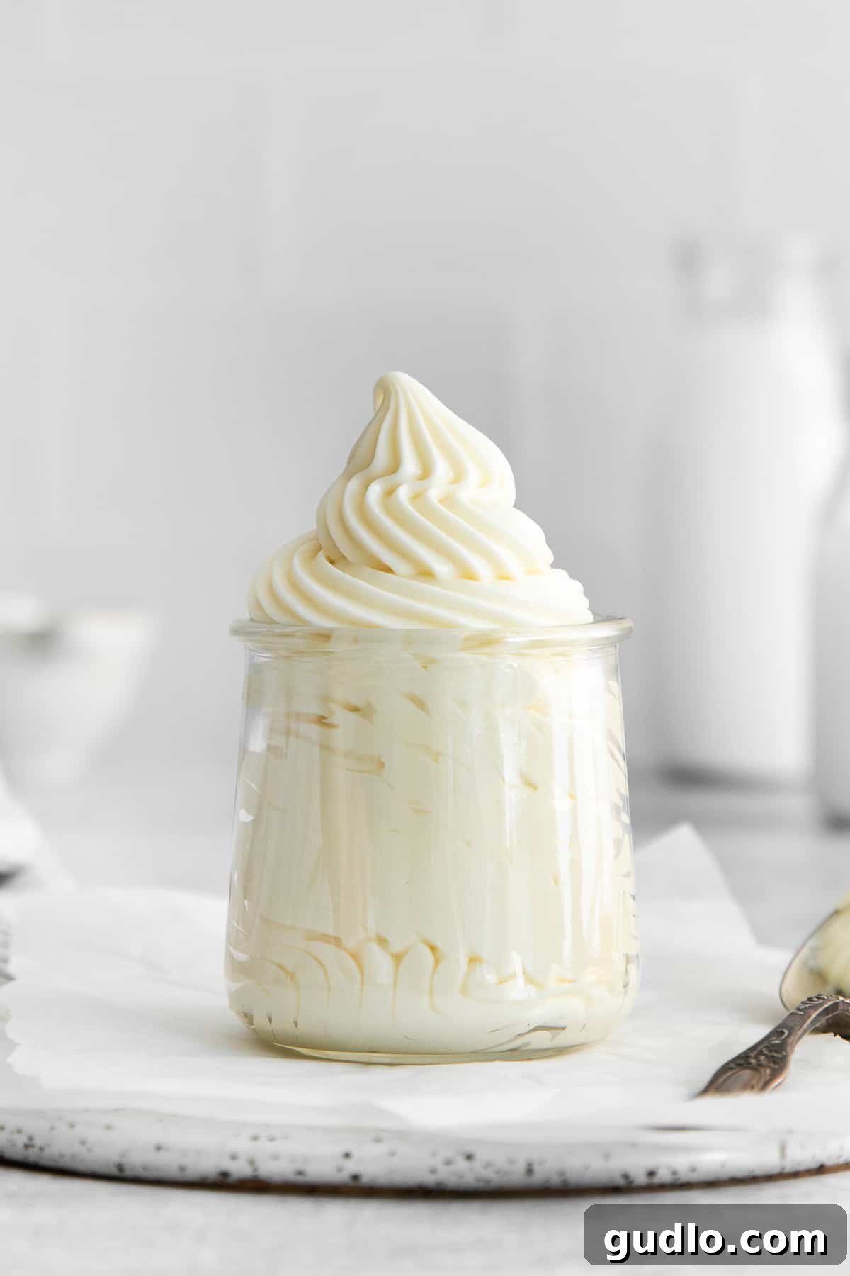 A jar brimming with homemade whipped cream cheese frosting, showcasing its thick and creamy texture, ready to be spread or piped onto your favorite desserts.