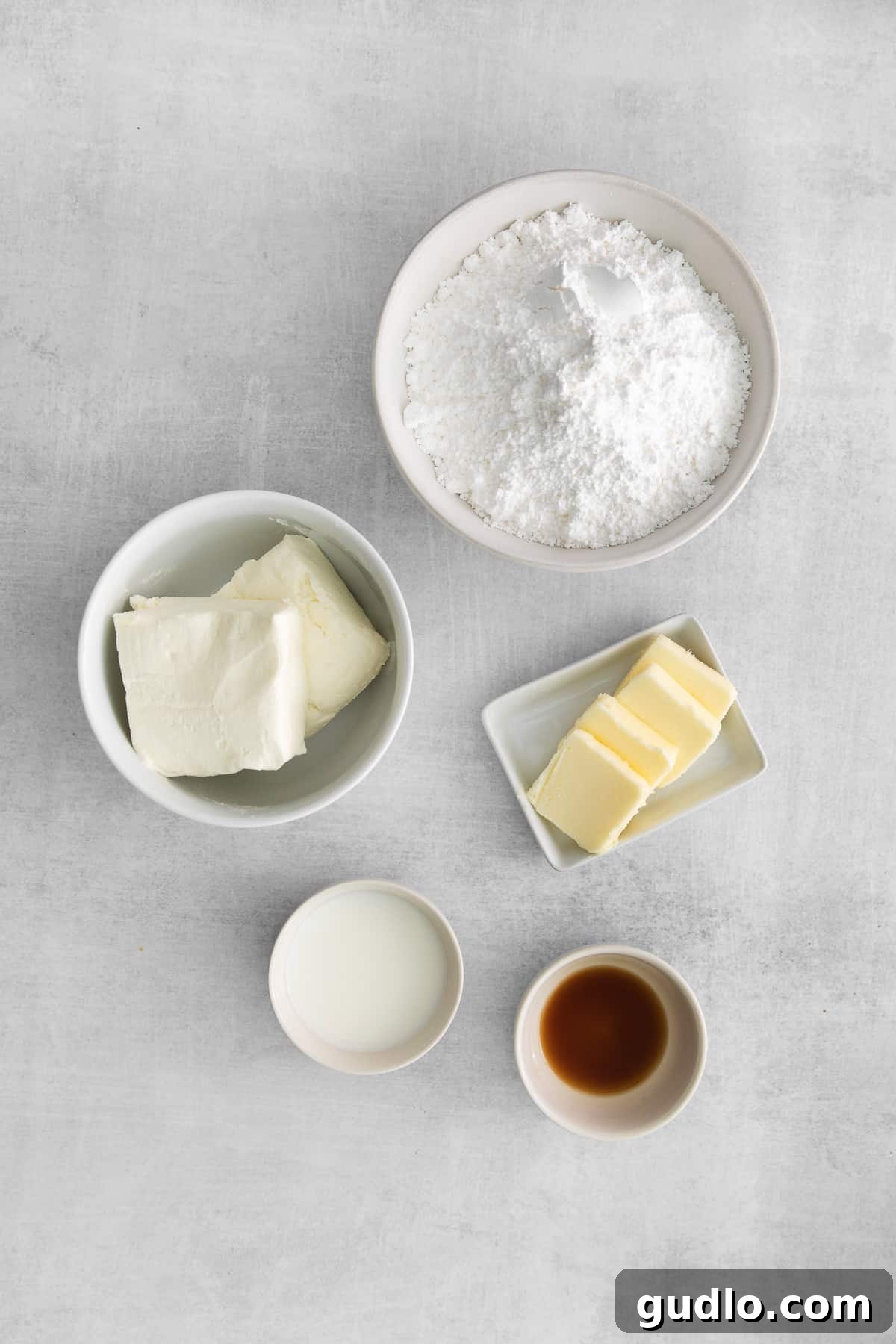 Five essential ingredients for making the ultimate whipped cream cheese frosting, neatly arranged in small bowls, ready for mixing.