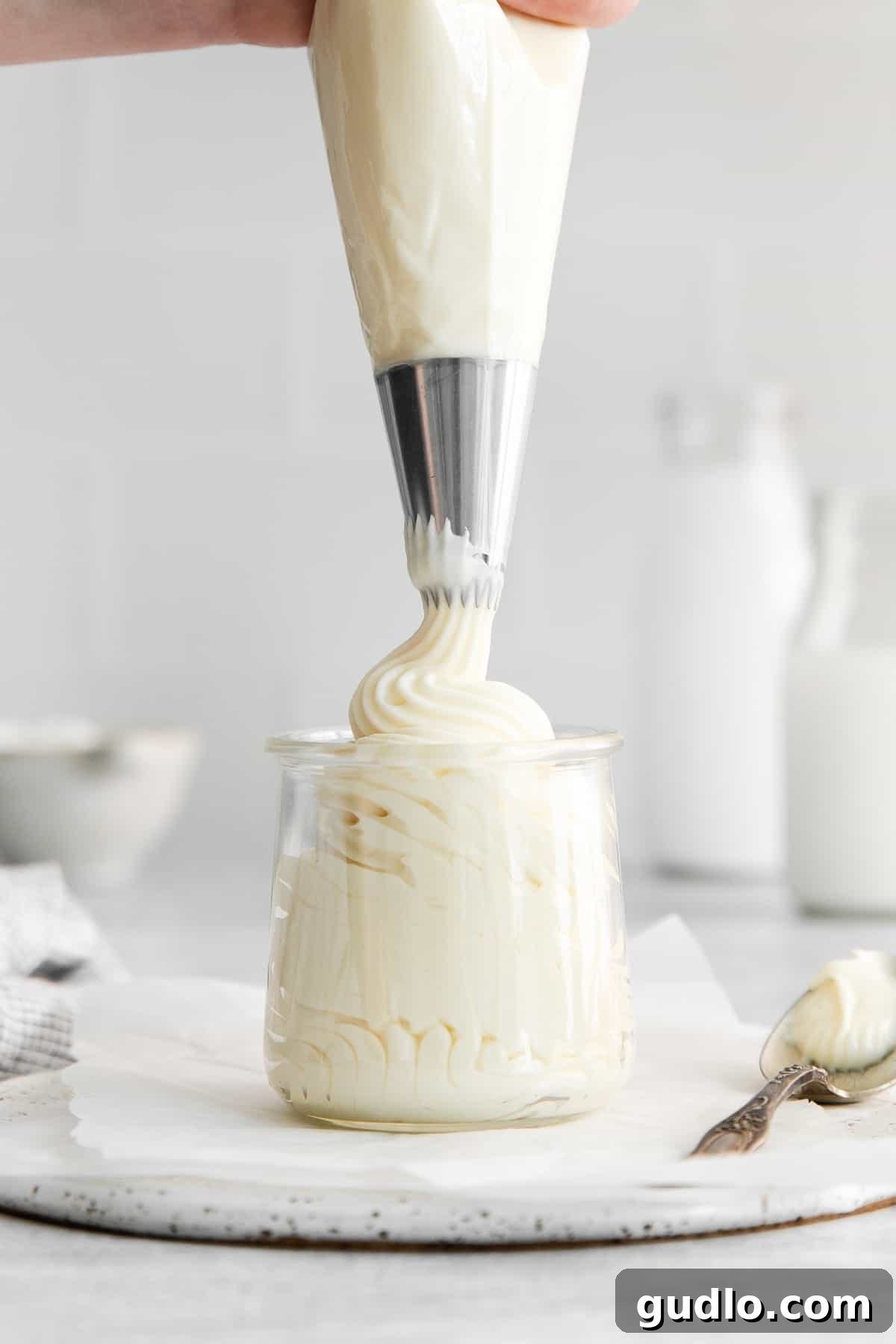 Whipped cream cheese frosting being expertly piped into a glass jar, demonstrating its perfect consistency for intricate decorations and storage.