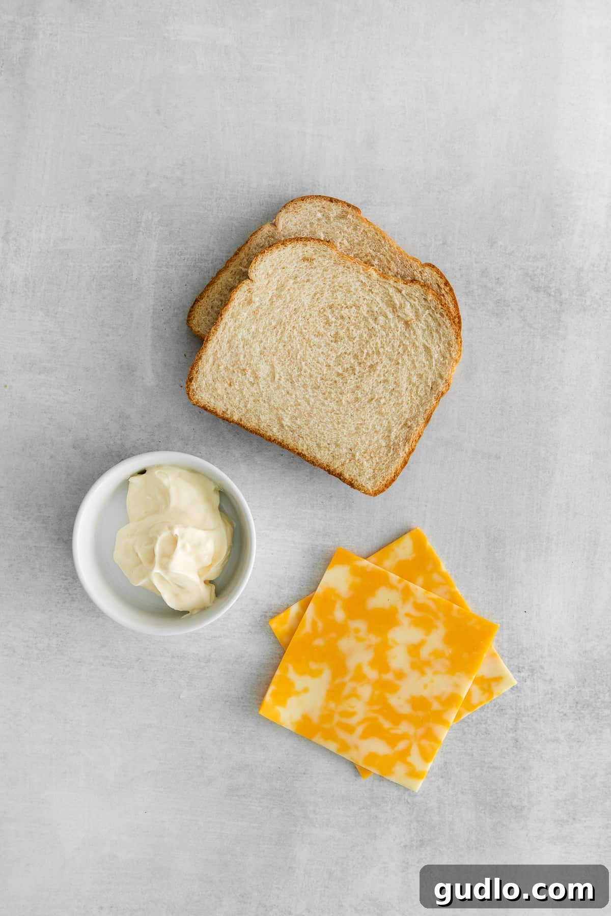 Essential Ingredients for Your Mayo Grilled Cheese Essential ingredients for grilled cheese with mayo neatly arranged on a white plate: two slices of bread, two slices of Colby Jack cheese, and a dollop of creamy mayonnaise.