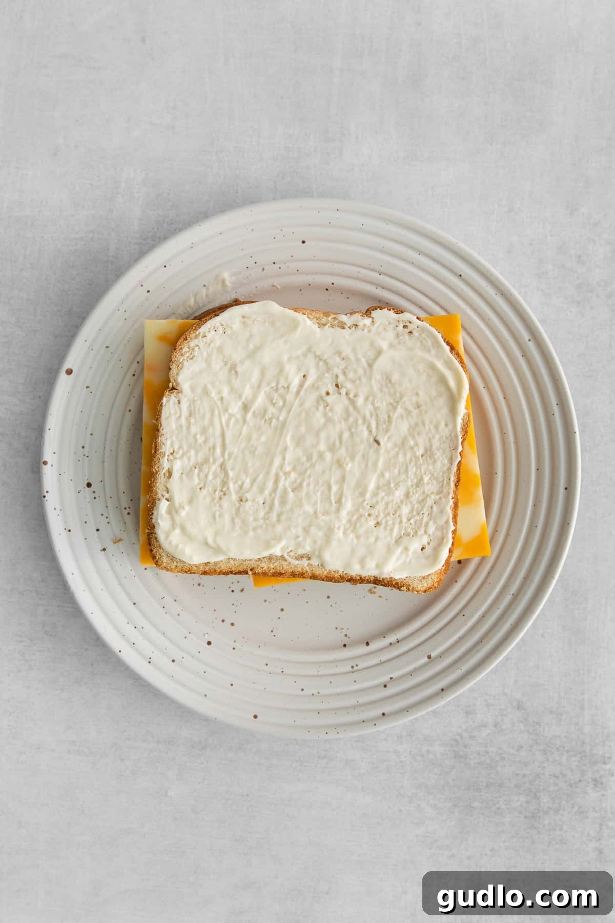 Mayonnaise: The Key to a Golden Crust A slice of bread generously topped with creamy mayonnaise, perfectly prepared and ready for the cheese layer of the sandwich.