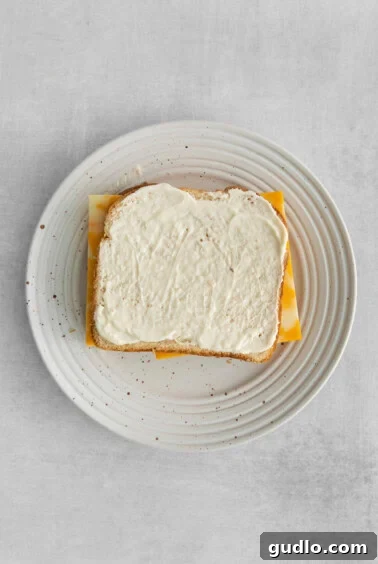 A slice of bread with mayonnaise generously spread on one side, ready for the cheese layer.