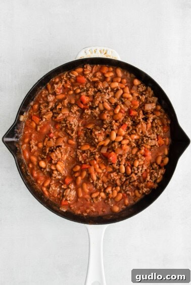 The beef and bean mixture simmering in the skillet, infused with taco seasoning and tomato sauce.