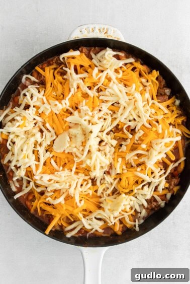 A skillet filled with the taco meat and bean mixture, generously covered with a layer of shredded cheese, ready for baking.