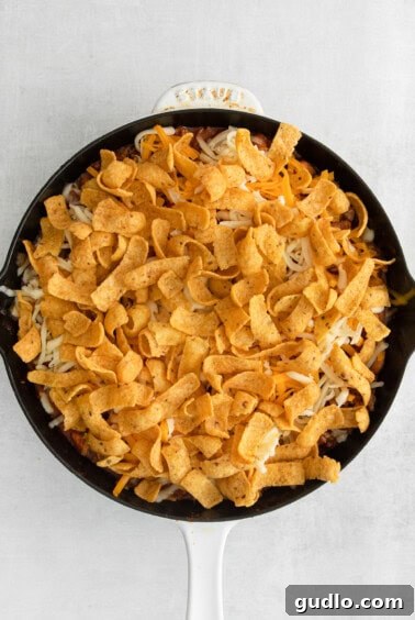The skillet now topped with a thick layer of Frito chips, completely covering the cheese and meat mixture beneath.