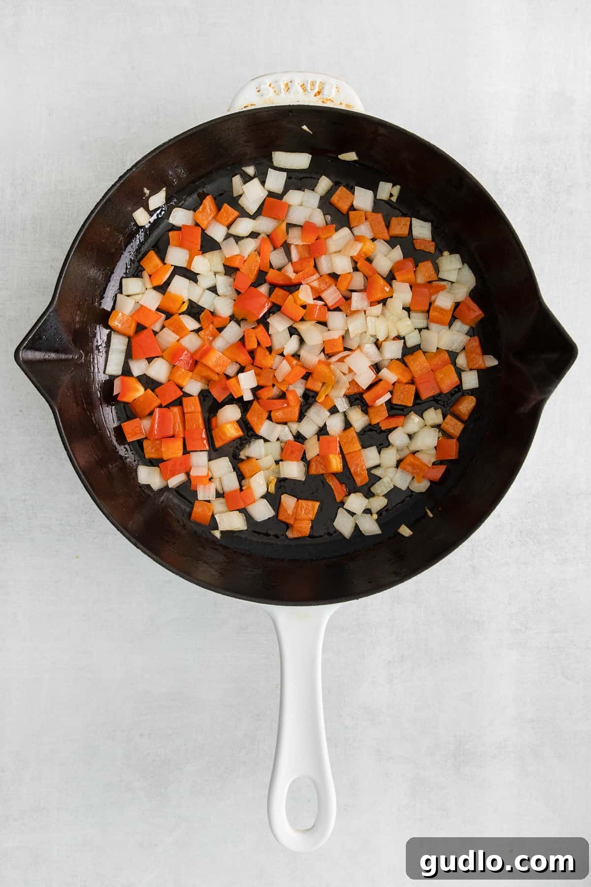 Sautéing Vegetables for a Flavorful Taco Skillet Finely diced red bell peppers and yellow onions gently sauteing in a large oven-safe skillet on the stovetop.