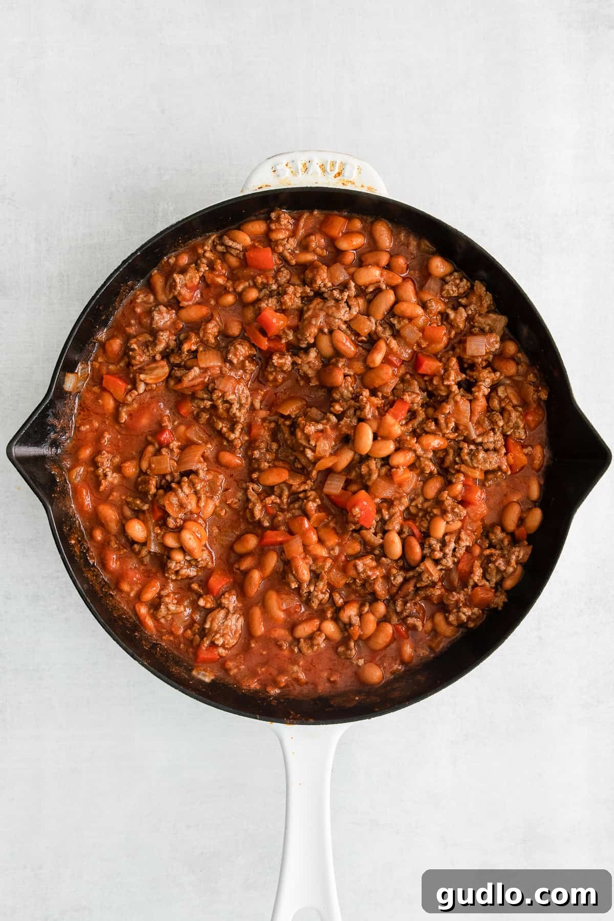 Simmering Cheesy Frito Taco Skillet Filling Rich Cheesy Frito Taco Skillet filling, a blend of ground beef, beans, and tomato sauce, gently simmering in a large skillet, creating a mouth-watering aroma.