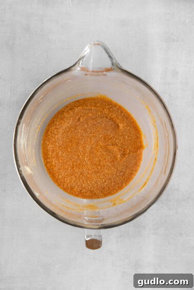 A glass bowl filled with a red-orange mixture, showing pumpkin puree and milk being added to the batter.