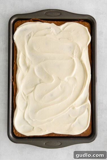 A pan of pumpkin bars generously covered with smooth, white cream cheese frosting, ready to be cut.