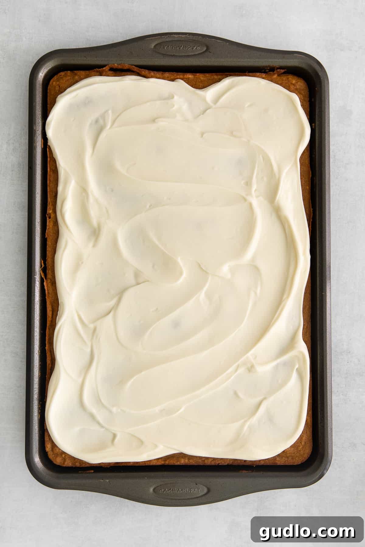 A baking pan filled with freshly frosted pumpkin bars, cut into neat squares, glistening with creamy white frosting.