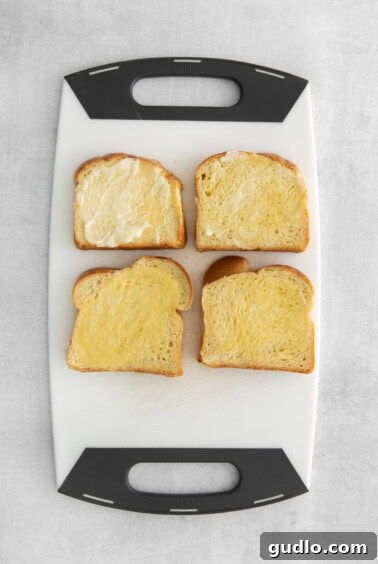 Decadent Strawberry Cheesecake French Toast 11 Four slices of brioche bread on a white cutting board, with butter spread on one side of each.