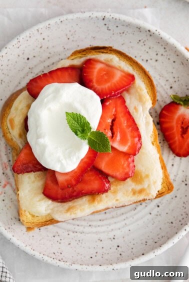 Decadent Strawberry Cheesecake French Toast 14 A plate featuring a slice of strawberry cheesecake French toast, generously topped with whipped cream and fresh strawberries.
