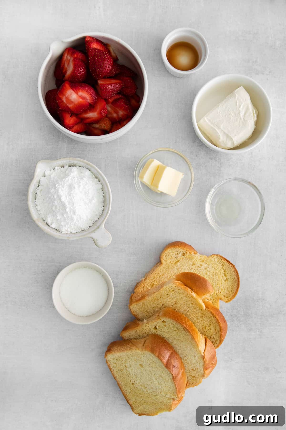 Decadent Strawberry Cheesecake French Toast 3 An array of fresh ingredients for strawberry cheesecake french toast, including strawberries, cream cheese, sugar, vanilla, brioche bread, and butter.