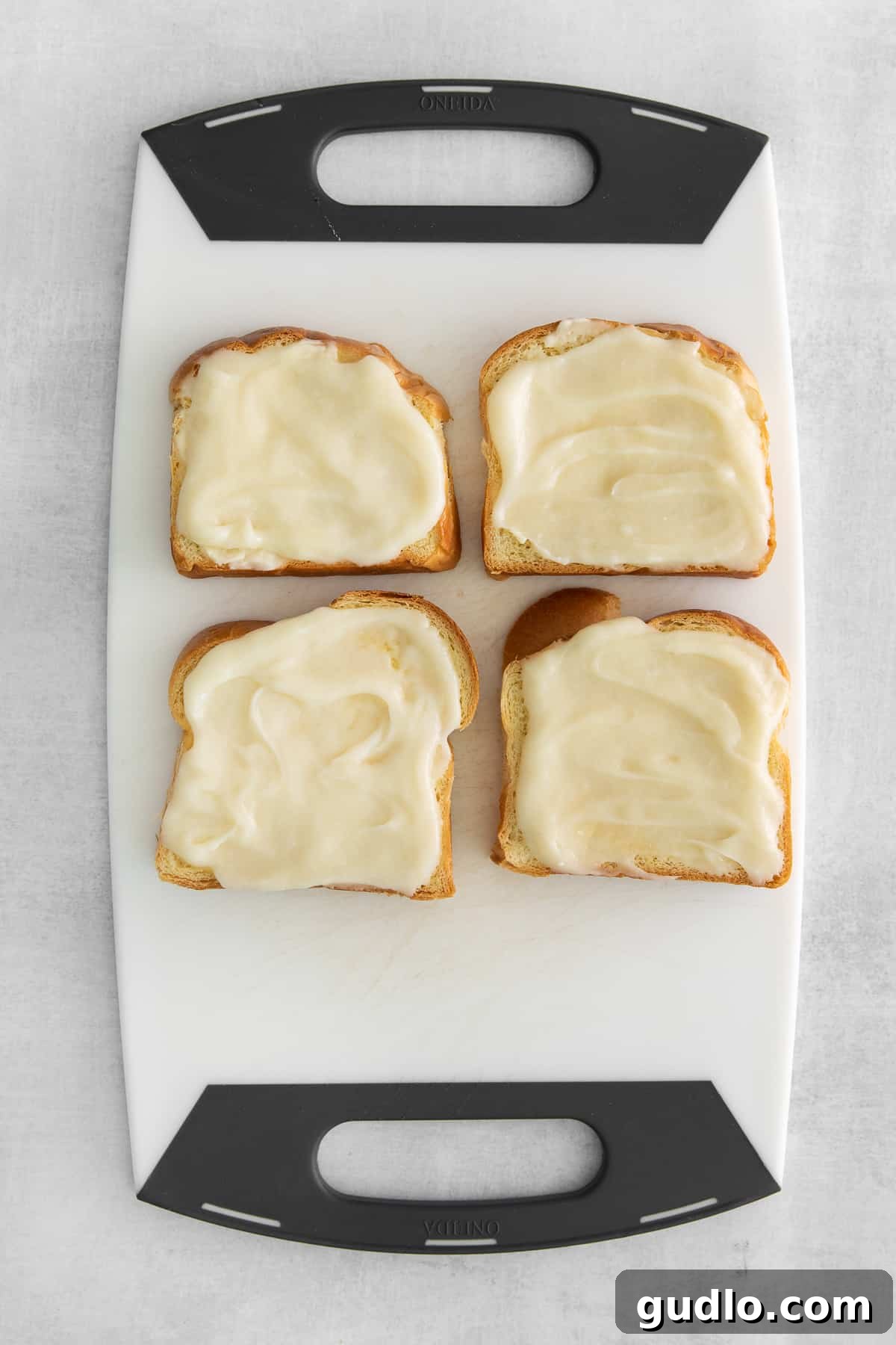 Decadent Strawberry Cheesecake French Toast 5 Four slices of brioche bread generously topped with a creamy white cheesecake mixture on a white cutting board.