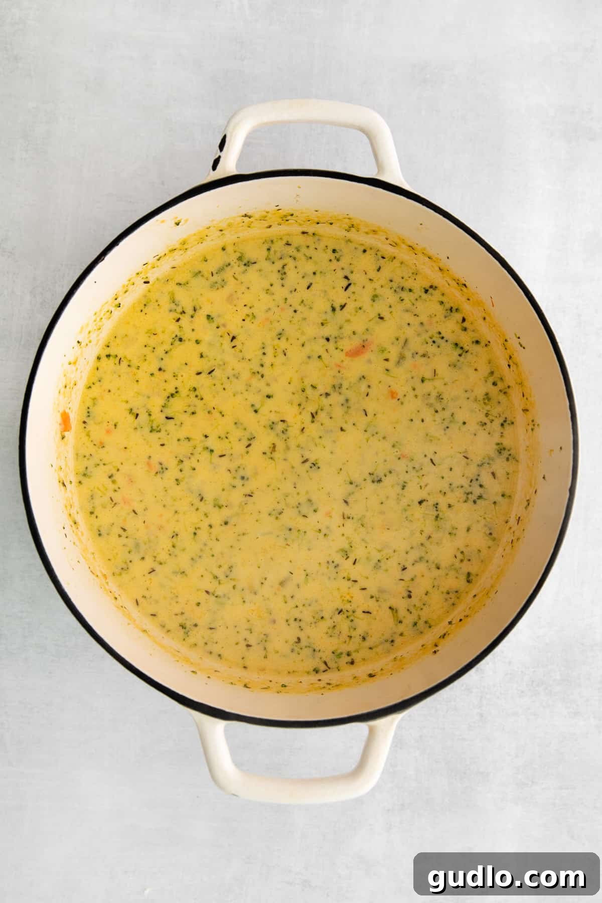 Broccoli potato cheese soup simmering gently in a large pot on the stove, indicating it's nearly ready to serve, with a visibly thick and creamy texture.