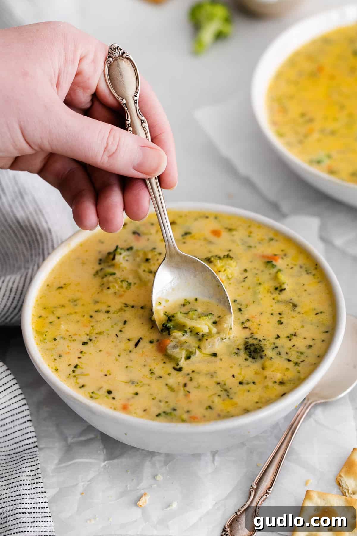 A spoon expertly scooping a hearty portion of the creamy broccoli potato cheese soup from a bowl, showcasing its rich texture and steam.