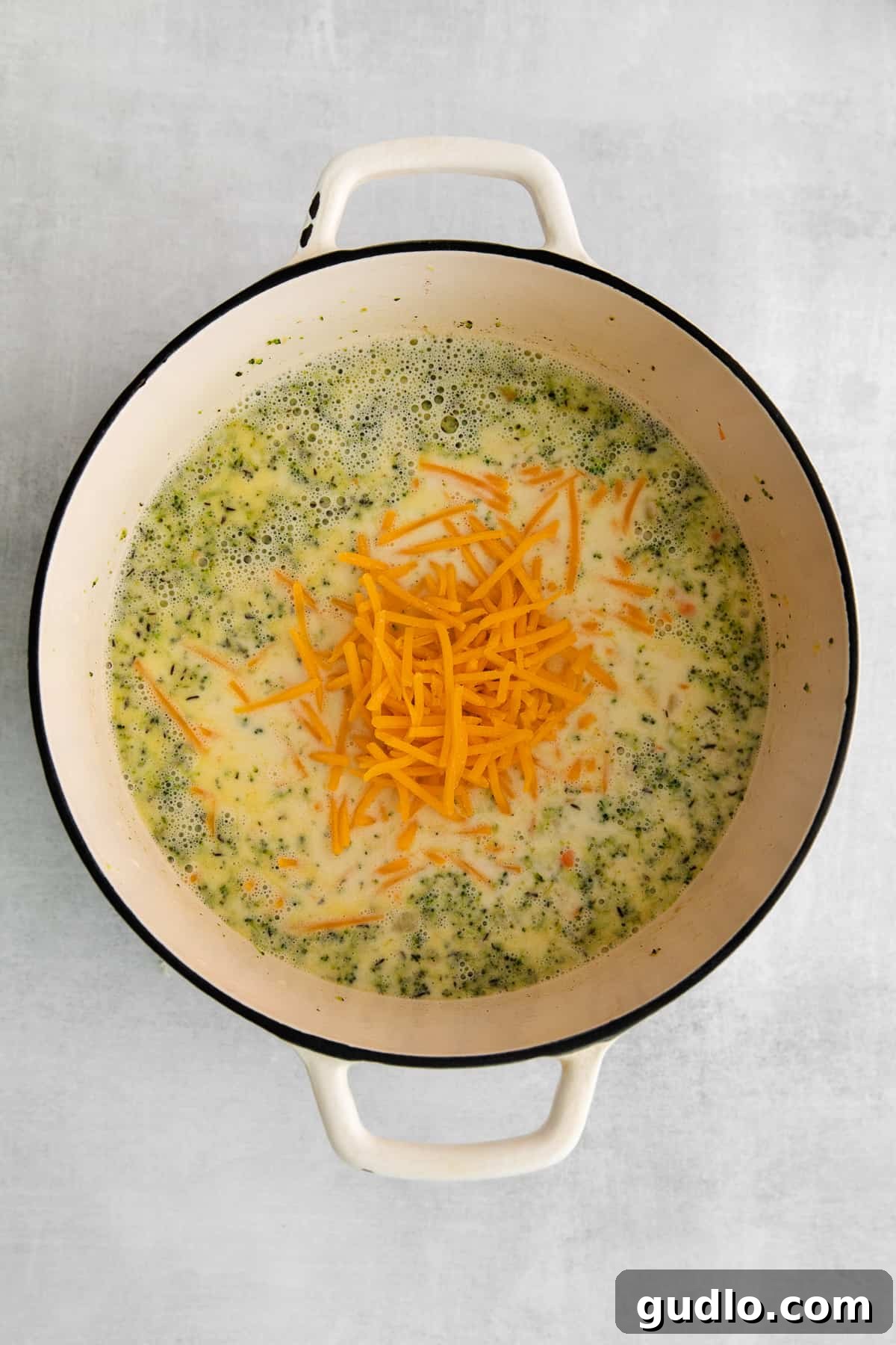 A skilled hand adding a generous amount of freshly shredded cheddar cheese to the simmering soup in a pot, creating a beautiful swirl of rich, golden color.