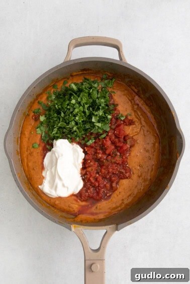 Adding Velveeta cheese and pico de gallo to the cooked chorizo in a skillet, mid-stir.